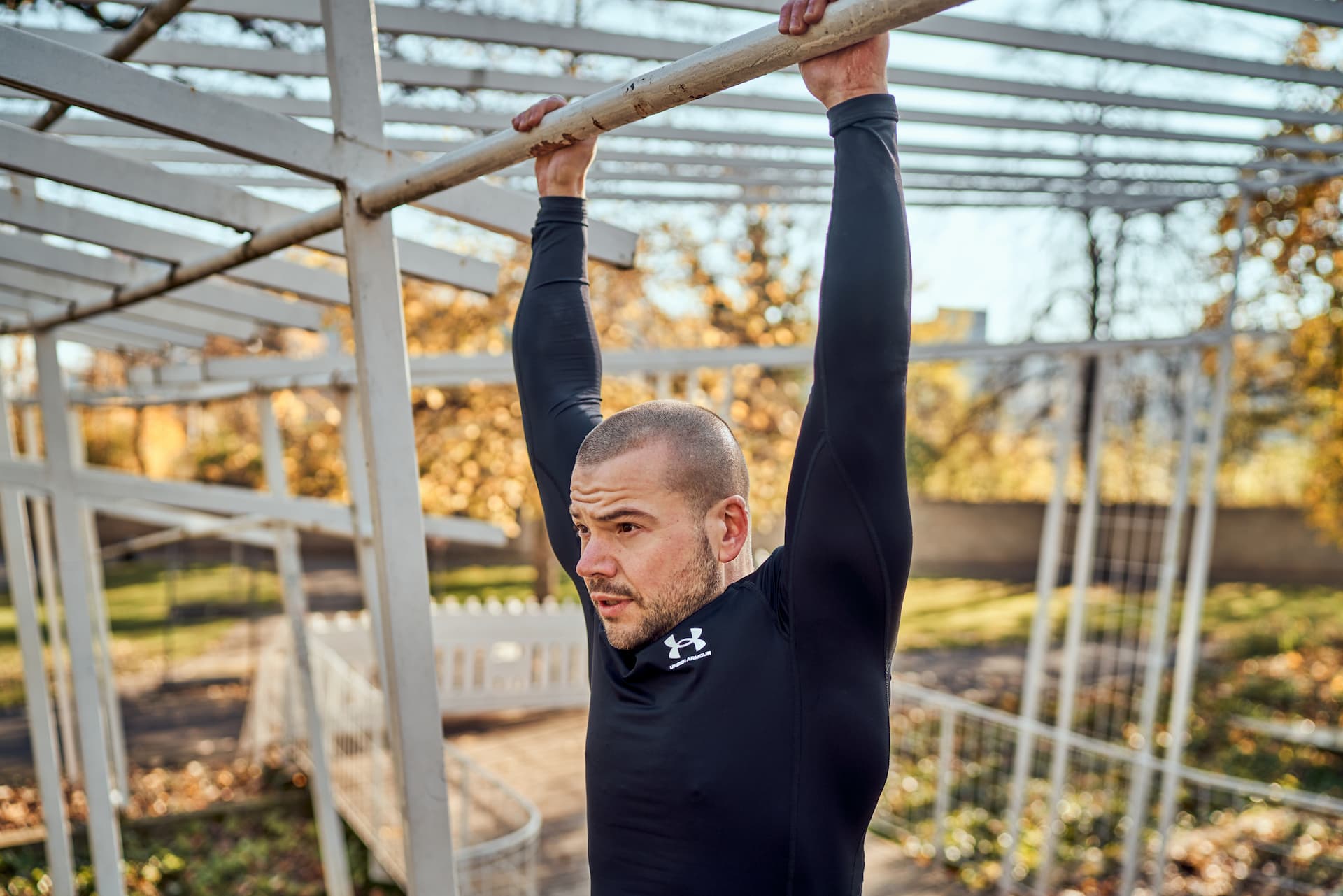 Personal Trainer hängt an einer Klimmzugstange beim Outdoortraining